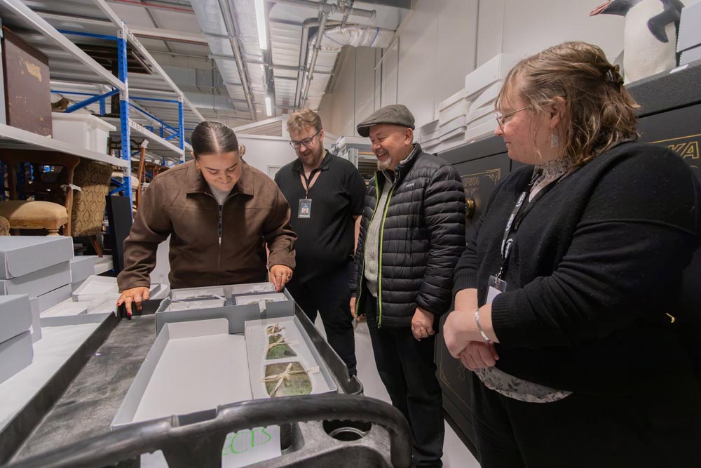 Te Unua Museum of Southland staff, from left, Tyra Ryan (Kaitiaki Mana Taoka), Ayden Dove (Registrar), Dougal Austin (Senior Curator – Māori), and Tiffany Jenks (Team Leader – Collections) view a patu pounamu once owned by Kāi Tahu rangatira Tūhawaiki at Te Pātaka Taoka Southern Regional Collections Facility. The patu was placed in the care of the former Southland Museum and Art Gallery by Naina Kihau Russell in 2001.